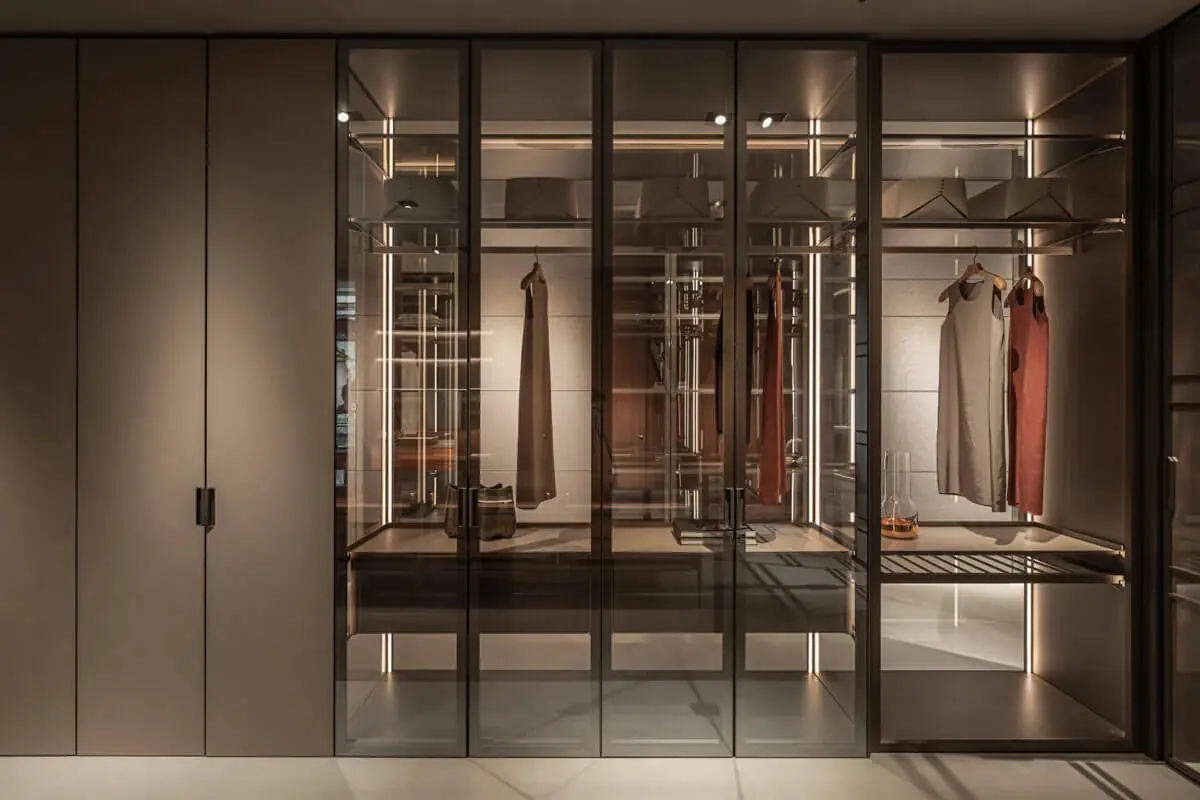 義大利半開放式衣櫃設計，茶色玻璃門片整合 LED 燈帶與吊掛層架，兼具展示感與防潮功能的更衣室收納系統
